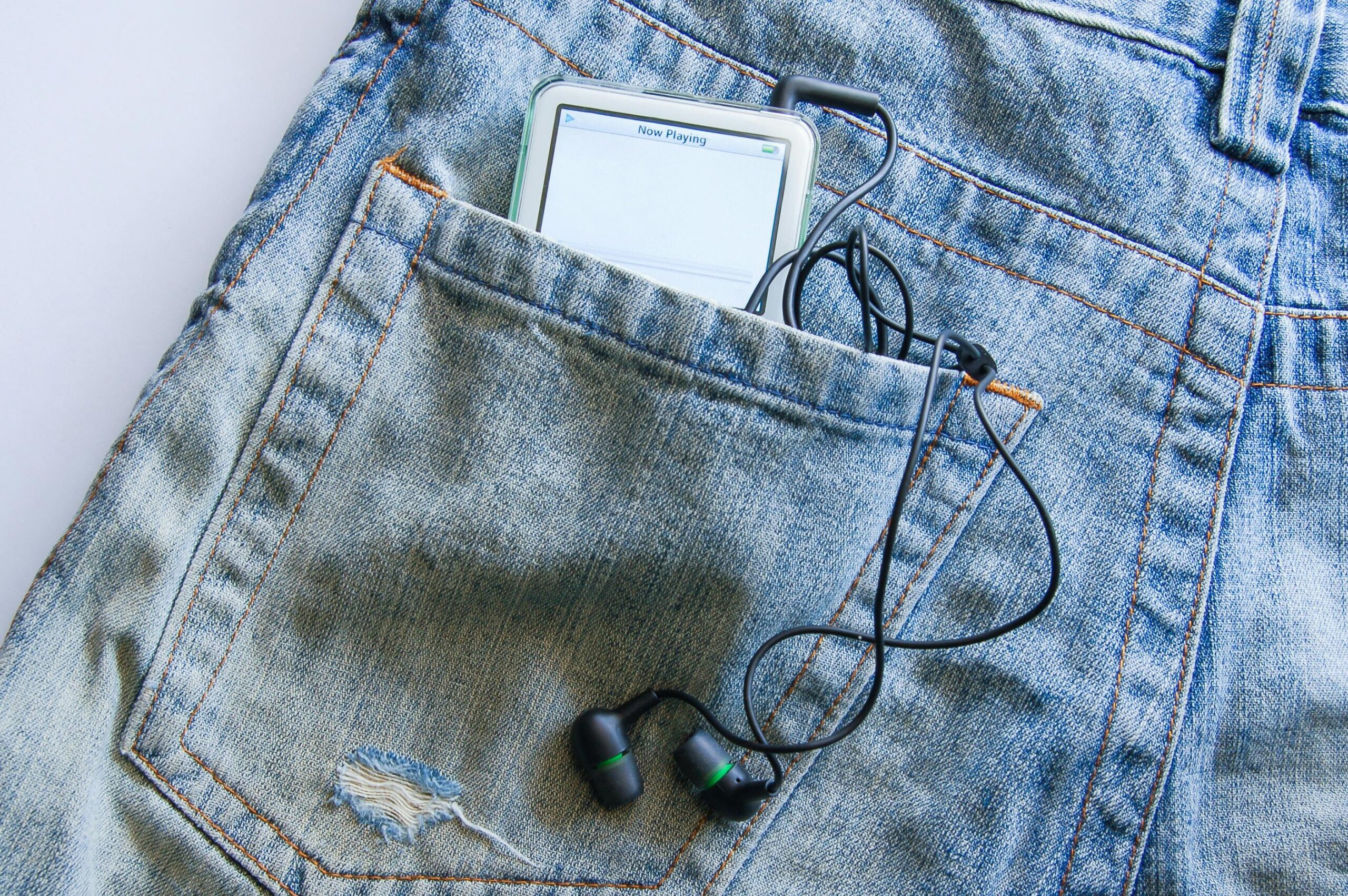 Modern smartphone with earphones in blue denim pocket, showcasing casual lifestyle.